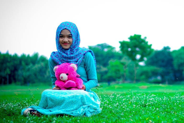 Young girl wearing a headscarf holding a stuffed toy bear