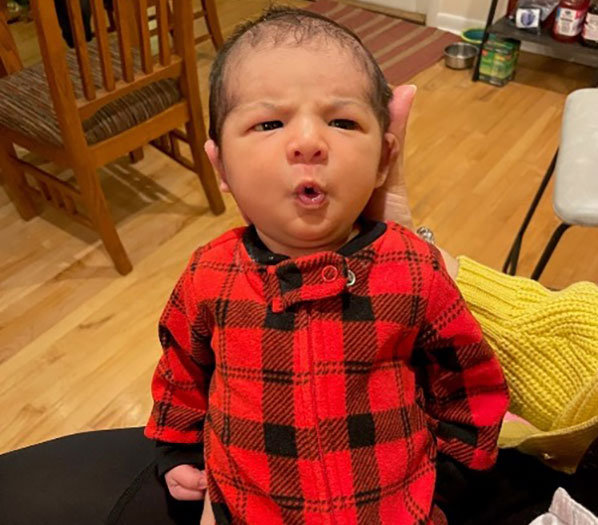 A picture of someone holding a baby, dressed in a red-and-black flannel jumper.