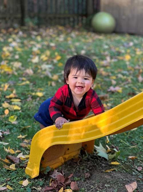 A toddler is pictured by a yellow, plastic slide.