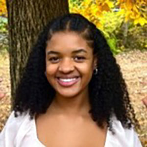 A headshot of Myah Anne Clayborn, who wears a white shirt and poses outside.