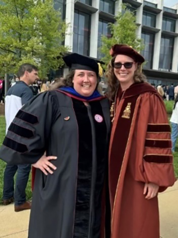 Professors Beardall and Mueller pose at graduation, dressed in their caps and gowns.