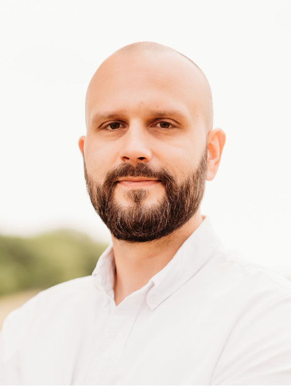 A headshot of Spencer Headworth, who wears a white dress shirt and poses outside.