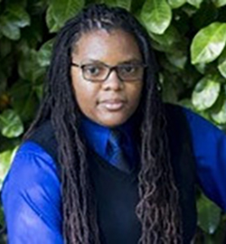 A headshot of Alyasah Sewell, who wears a blue dress shirt and vest.