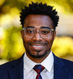 A headshot of Rashawn Ray, who wears a dark suit and tie.