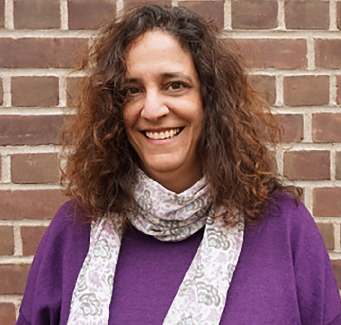 A headshot of Melissa Milkie, who wears a purple sweater and a scarf.