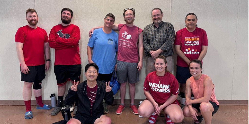 A co-ed group of nine people in athletic clothes pose after a game, with most wearing red IU-themed shirts.