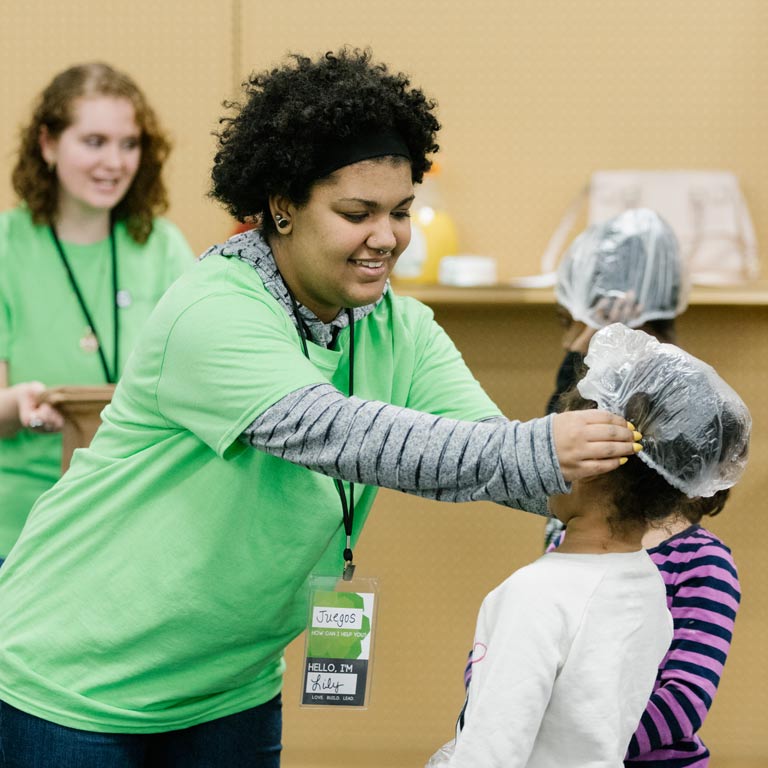 WOKE club member helps young girl put a shower cap on for an activity