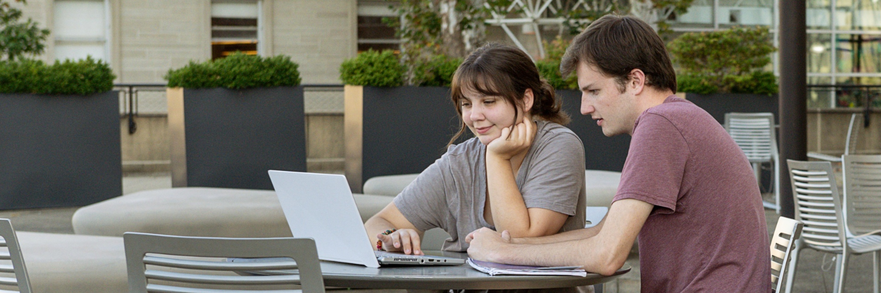 Students working outside campus courtyard together over a laptop.